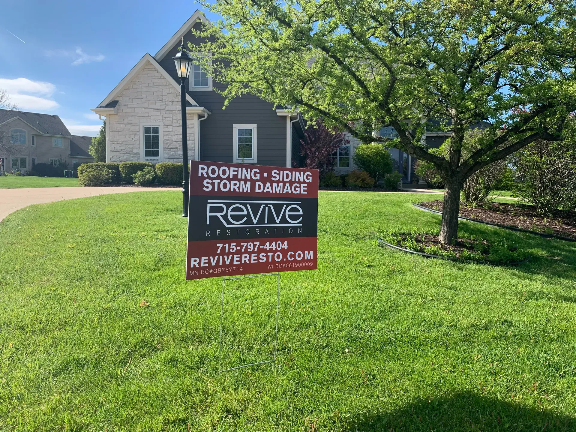 Revive Roofing & Restoration yard sign on the lawn of a stone-and-siding home