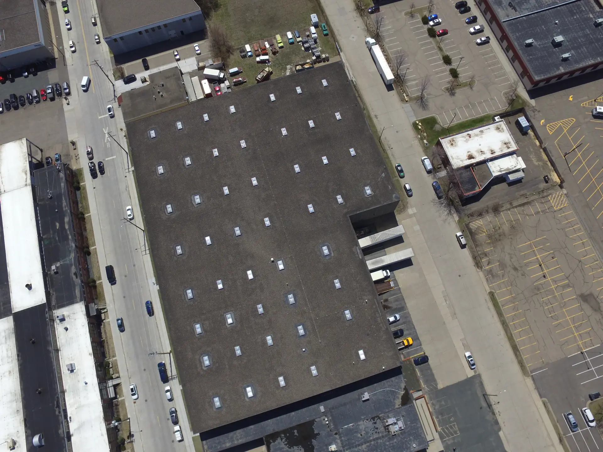 Overhead view of a flat commercial roof on a warehouse, ringed by parking and loading bays