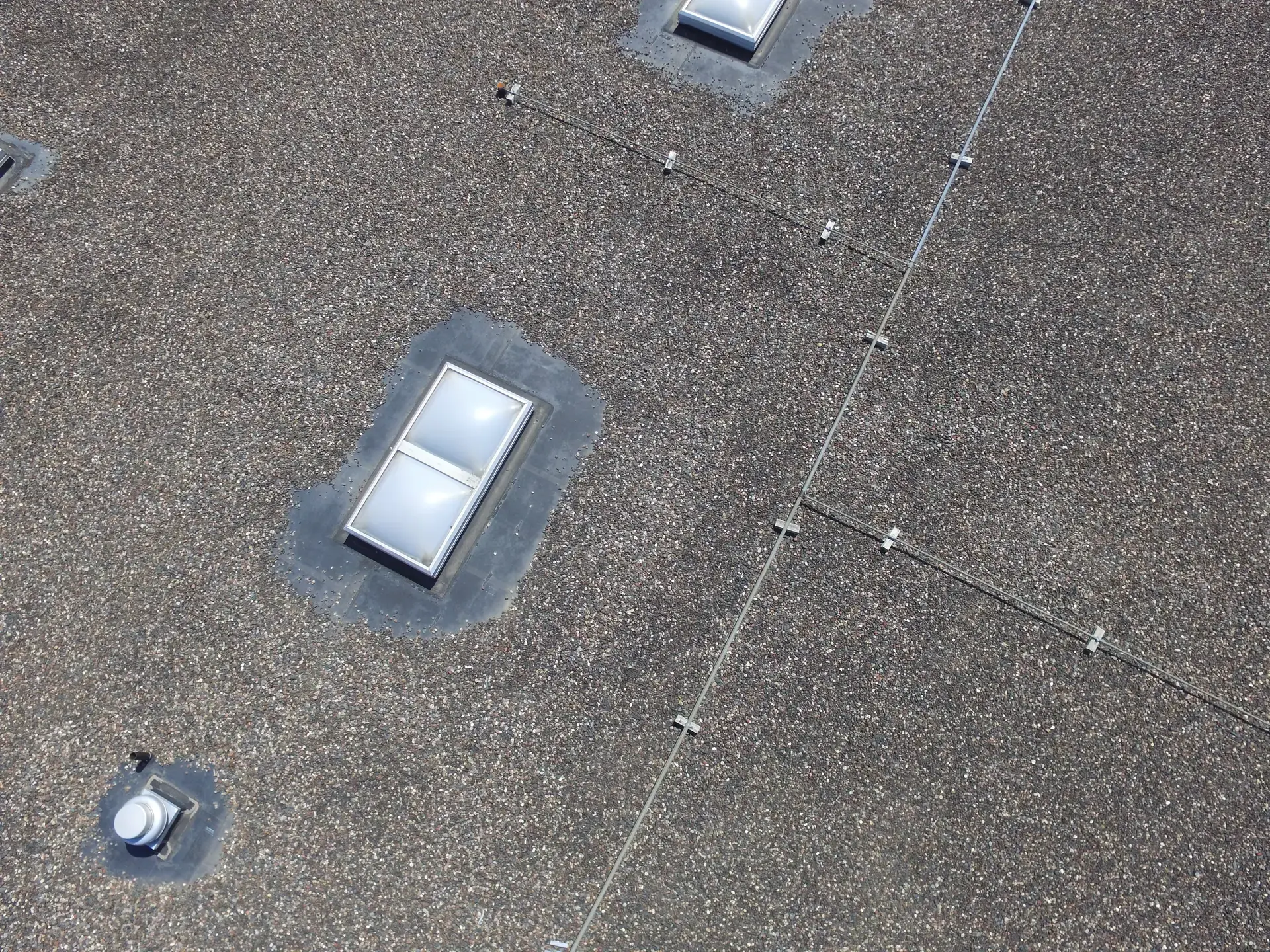 Overhead view of skylights and seams on a gravel-surfaced flat commercial roof
