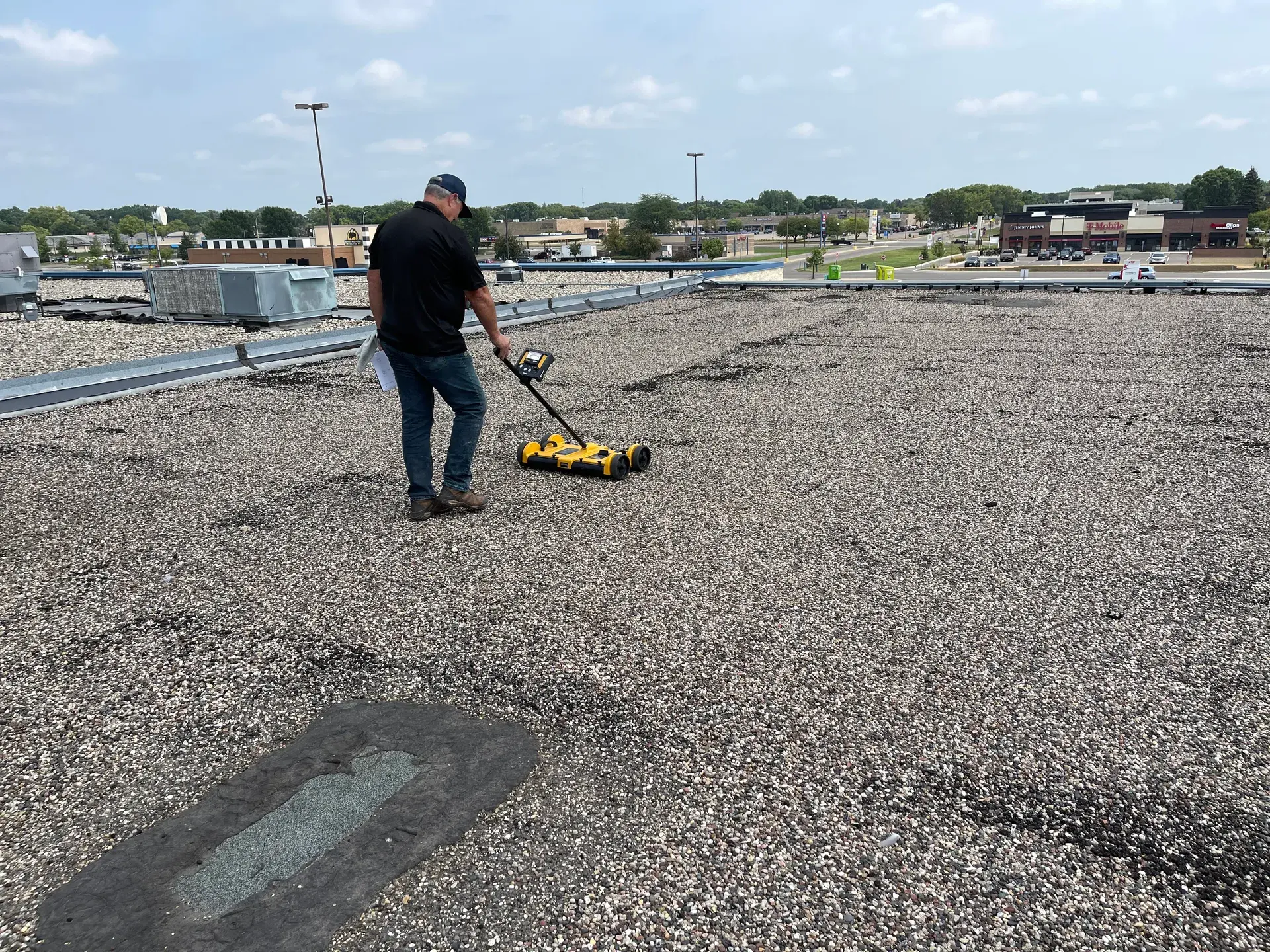 Roofer walking a gravel-surfaced flat commercial roof with a rolling tool