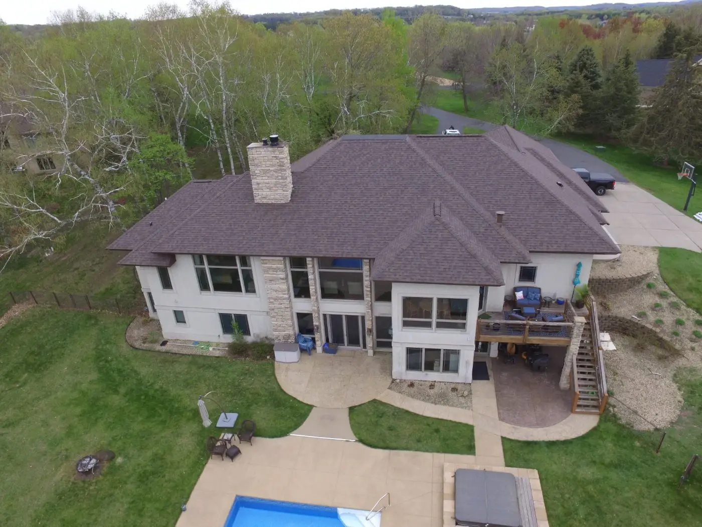 Completed brown asphalt shingle roof on a large stucco and stone home, seen from above