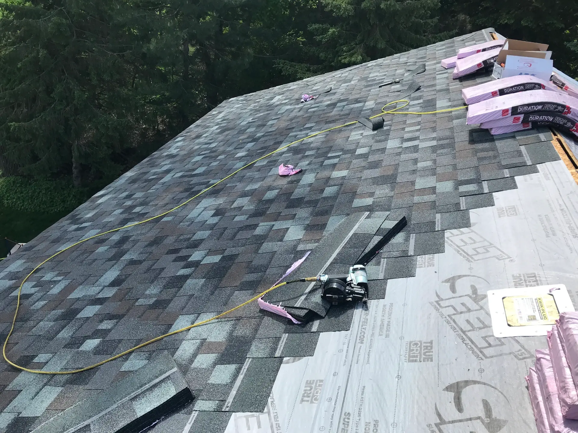 New shingles going down over synthetic underlayment, with bundles staged along the ridge