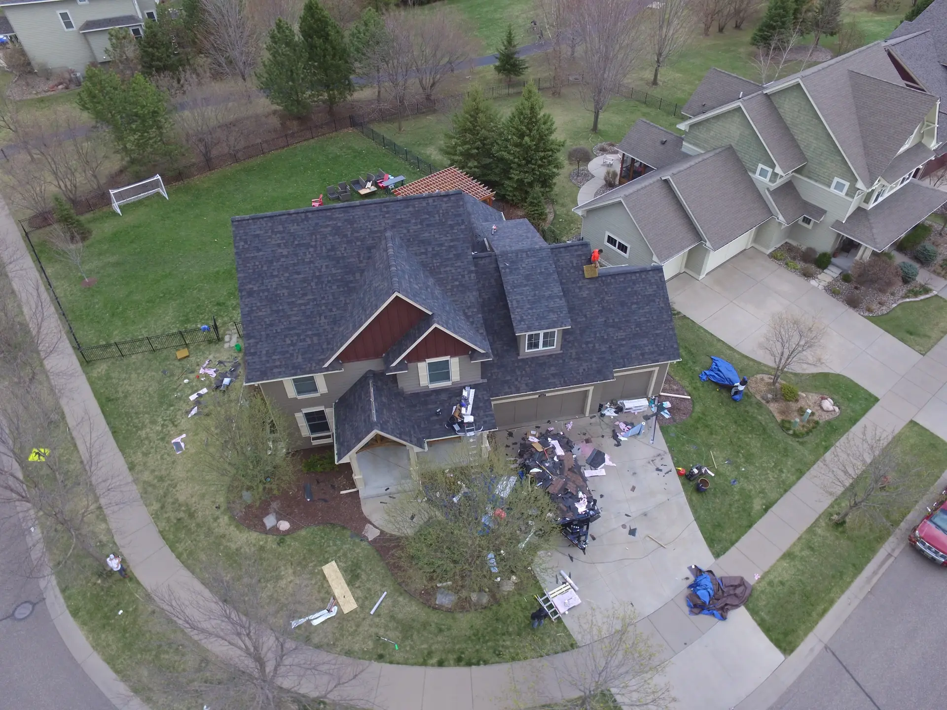 Aerial view of a roof replacement underway, with tear-off debris and materials across the driveway