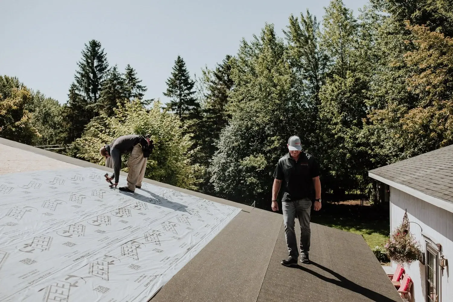 Two roofers laying underlayment across a residential roof