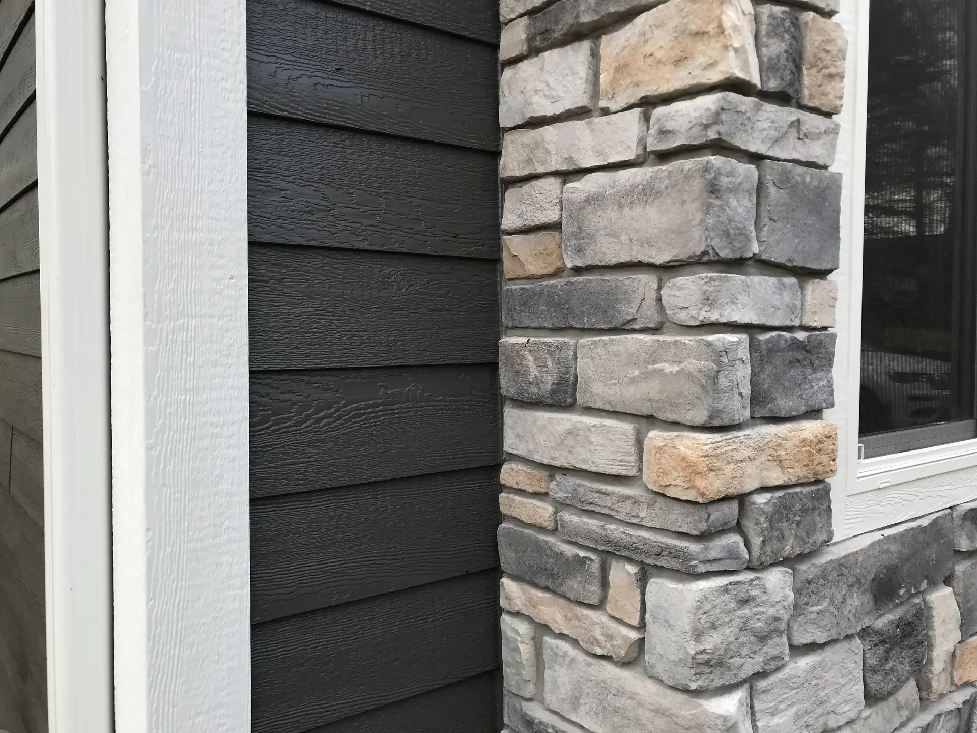 Corner where dark lap siding meets a gray stone veneer column