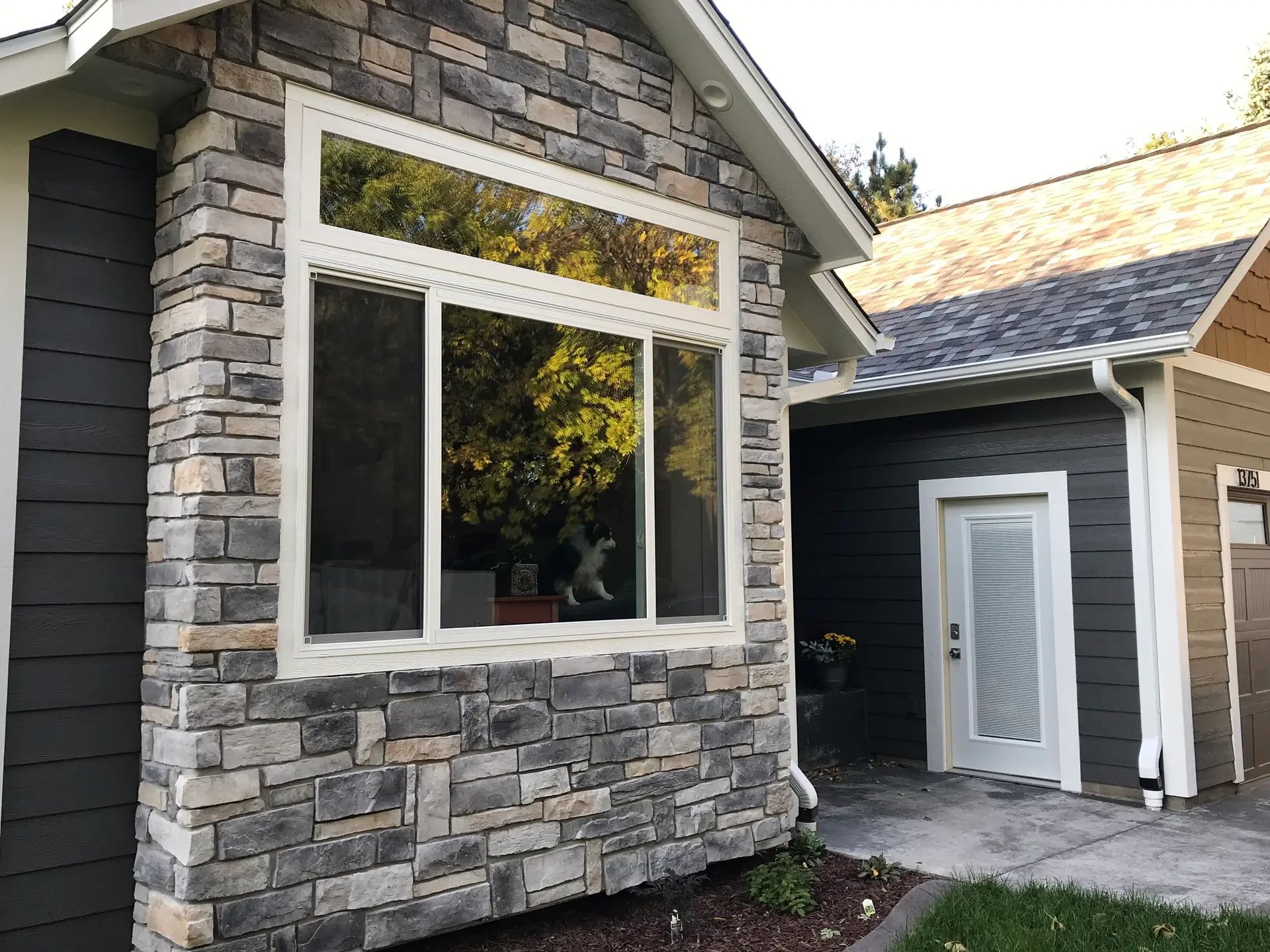 Picture window with white trim set into a stone and lap siding exterior